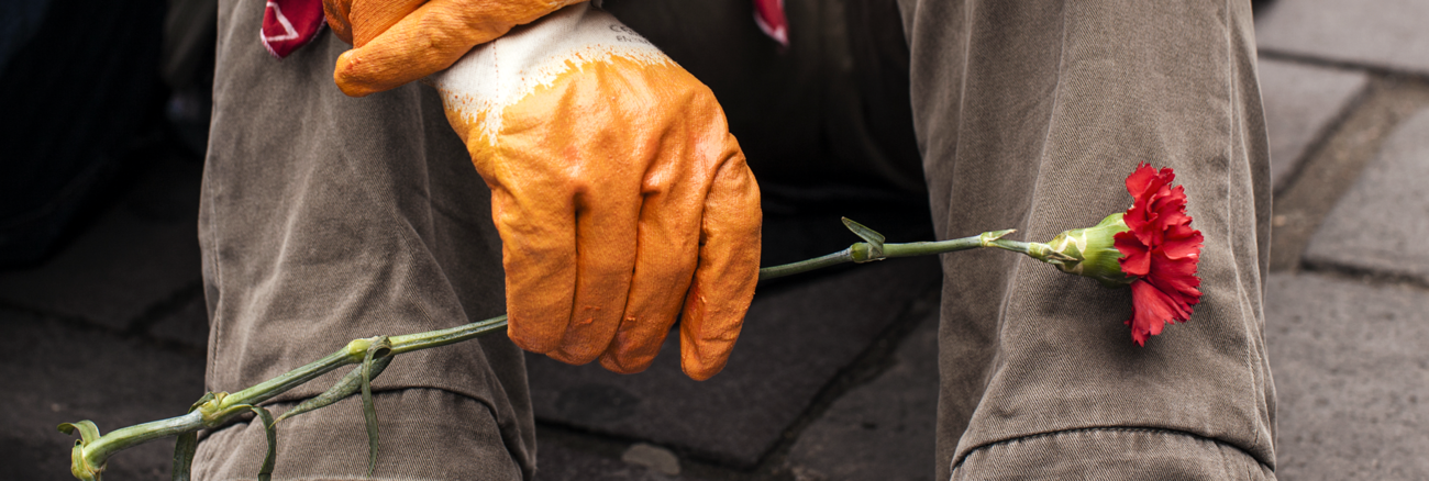 Ein Mann mit Arbeitshandschuhen hält eine Mai-Nelke © picture alliance/abaca Ein Mann mit Arbeitshandschuhen hält eine Mai-Nelke © picture alliance/abaca