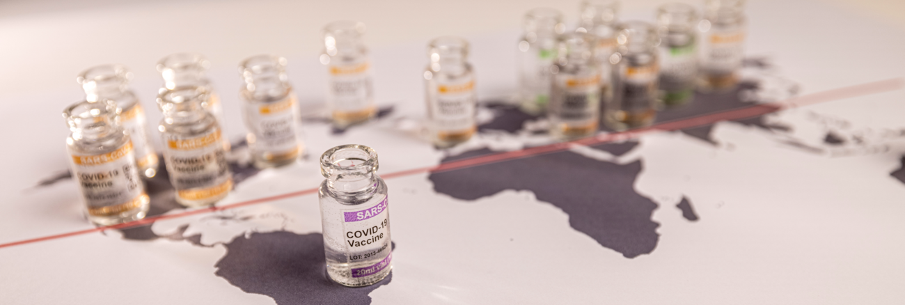 Impfdosen-Fläschchen stehen auf einer Weltkarte © iStock/FrankyDeMeyer