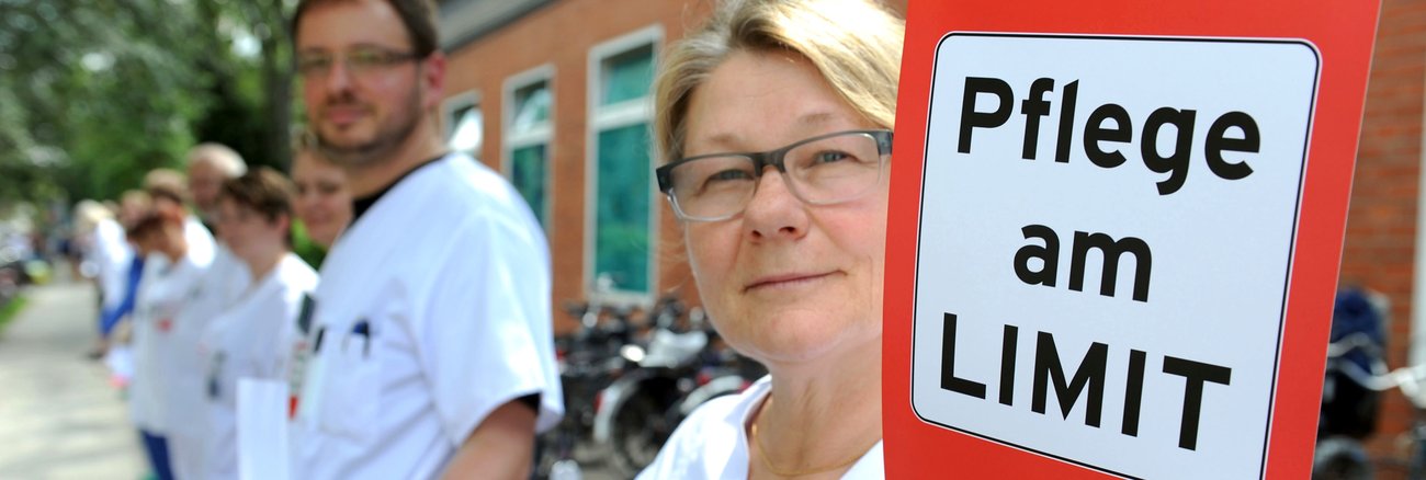 Eine von 200 Krankenschwestern in einer Menschenkette hält ein Schild mit der Aufschrift: Pflege am Limit © picture alliance/dpa|Carmen Jaspersen