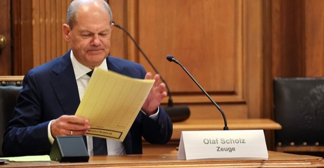Im Untersuchungsausschuss: Bundeskanzler Olaf Scholz hält eine Akte picture, vor ihm auf dem Tisch ein Schild mit der Aufschrift Olaf Scholz Zeuge © picture alliance/dpa|Christian Charisius