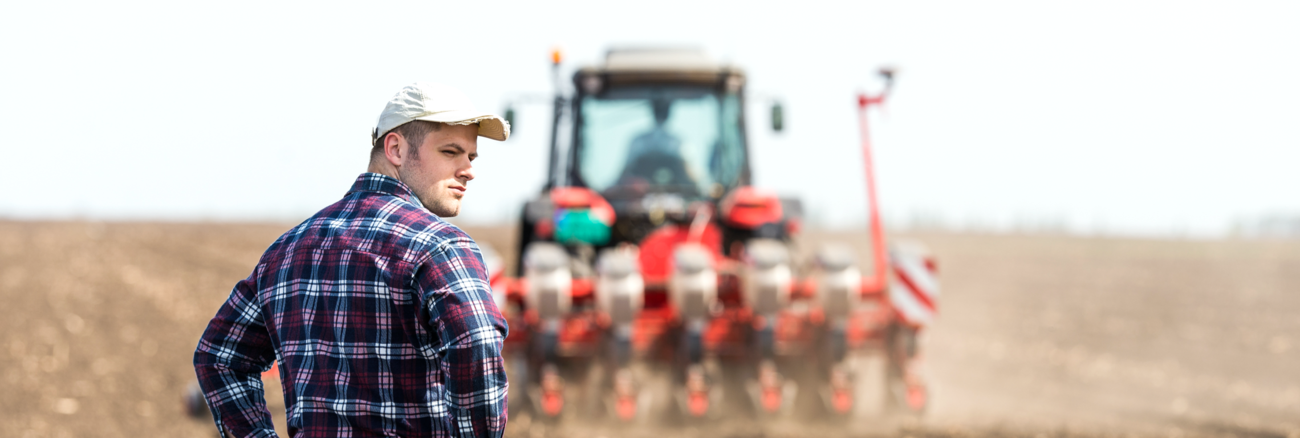 Junger Bauer auf einem Acker hinter einem Traktor bei der Aussaat © iStock/fotokostic