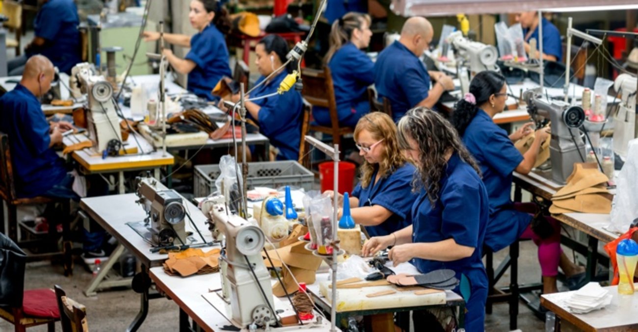 Frauen und Männer in blauen Kitteln arbeiten an Nähmaschinen in einer Fabrik @ iStock/andresr