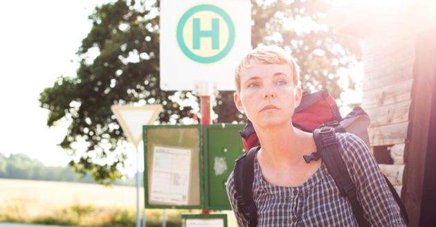 Eine junge Frau mit Rucksack an einer Bushaltestelle © iStock/lowkick