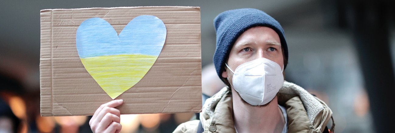 Ein Mann auf dem Berliner Hauptbahnhof hält ein Schild mit einem Herz in den Farben der ukrainischen Flagge. © picture alliance/SZ Photo|Jens Schicke