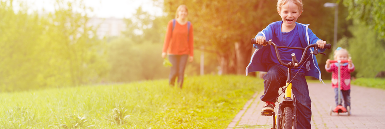 Ein Kind fährt lachend auf einem Fahrrad über einen Weg in einer Grünanlage. | Foto: © istock.com/Nadezhda1906