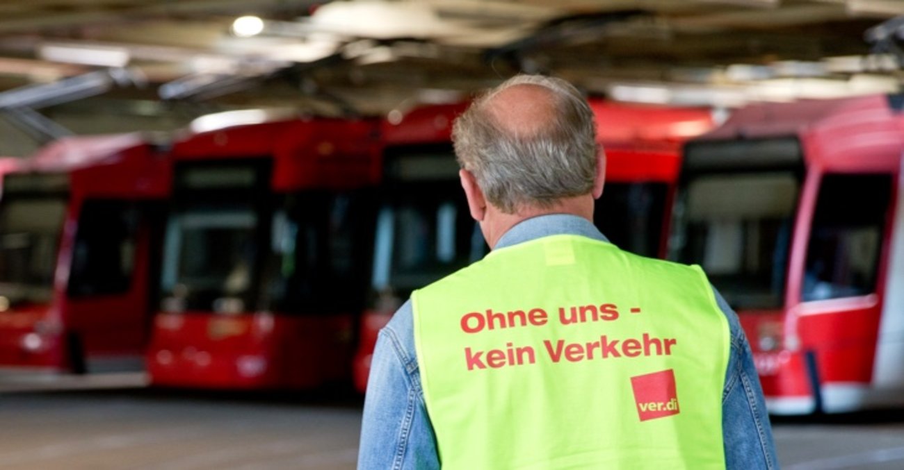 Ein Mann vor roten Straßenbahnen trägt eine gelbe Warnweste mit der Aufschrift: Ohne uns kein Verkehr © picture alliance/dpa|Daniel Karmann