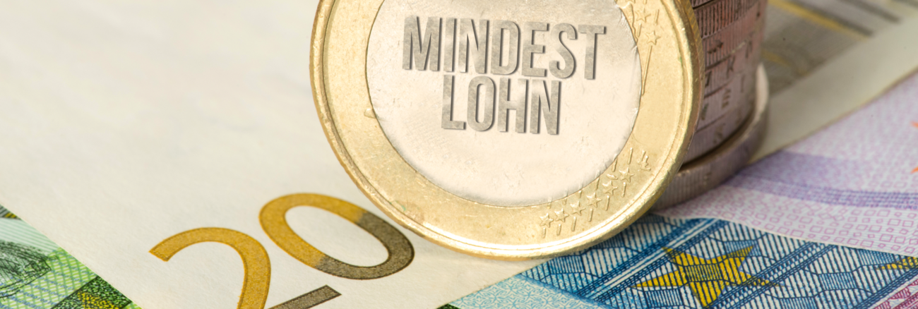 An einen Stapel Euro-Münzen ist eine gangelehnt mit der Aufschrift Mindestlohn © iStock/Stadtratte