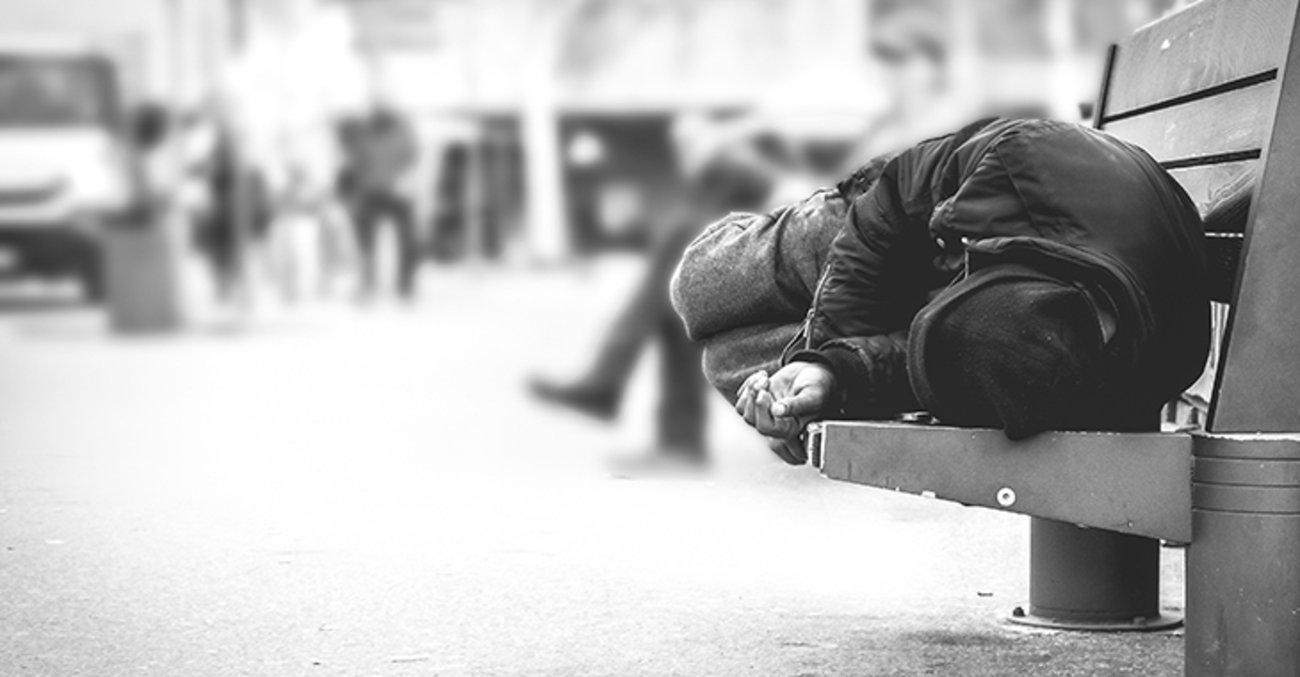 Eine wohnungslose Person liegt auf einer Bank der Straßenmöblierung einer Innenstadt und schläft. Foto: © istock.com/Srdjanns74
