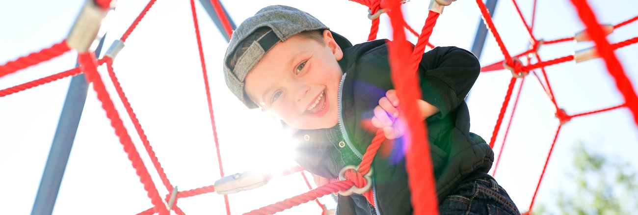 Lachender Junge in einem Kletternetz © iStock/LSOphoto