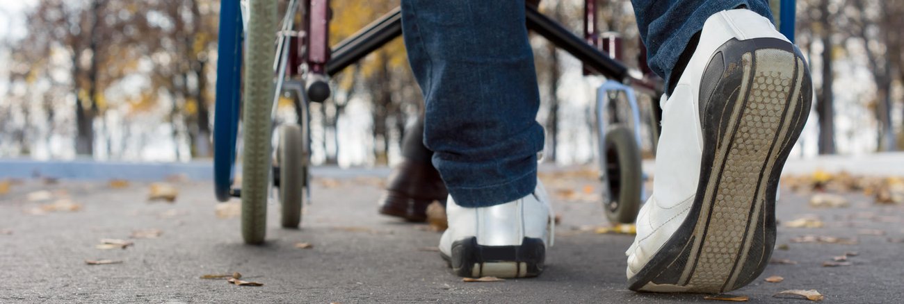Nahaufnahme von hinten zeigt die Schuhe einer Person, die einen Rollstuhl schiebt © iStockphoto.com/Vicheslav