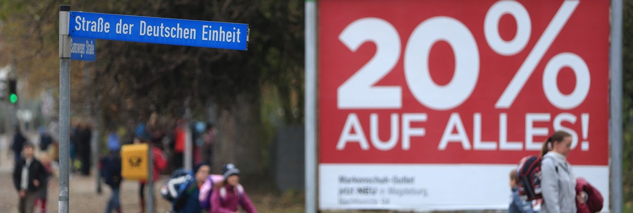 Passanten laufen in Wolmirstedt (Sachsen-Anhalt) an einem Straßenschild mit der Aufschrift »Straße der deutschen Einheit« vorbei © dpa