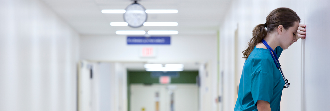 Eine erschöpfte Pflegekraft lehnt an der Wand eines Flurs im Krankenhaus. Foto: © istock.com/FangXiaNuo Eine erschöpfte Pflegekraft lehnt an der Wand eines Flurs im Krankenhaus. Foto: © istock.com/FangXiaNuo