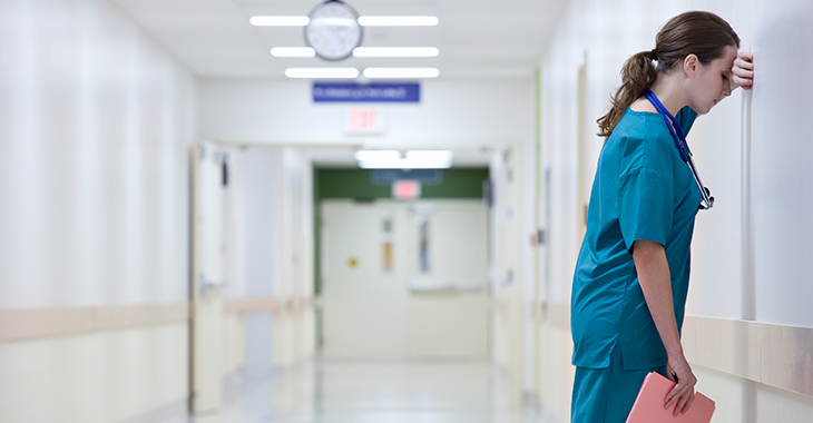 Eine erschöpfte Pflegekraft lehnt an der Wand eines Flurs im Krankenhaus. Foto: © istock.com/FangXiaNuo