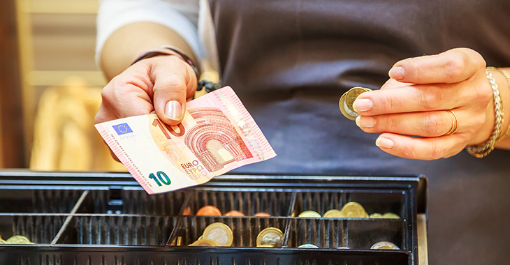 Kassiererin mit Geld in beiden Händen vor einer geöfffneten Kassenschublade © iStock/pixinoo