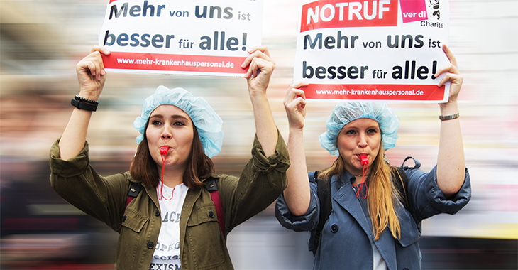 Berliner Pflegekräfte beim Pflegestreik der Charité halten Schilder hoch mit dem Slogan "Mehr von uns ist besser für alle!"