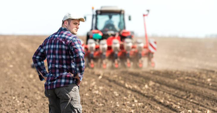 Junger Bauer auf einem Acker hinter einem Traktor bei der Aussaat © iStock/fotokostic