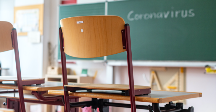 Stühle stehen auf den Tischen in einem leeren Klassenzimmer, an der Tafel steht Coronavirus © dpa/Armin Weigel