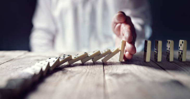 Ein Mann stoppt mit seiner Hand das Umfallen einer Domino-Kette © iStockphoto.com/BrianAJackson