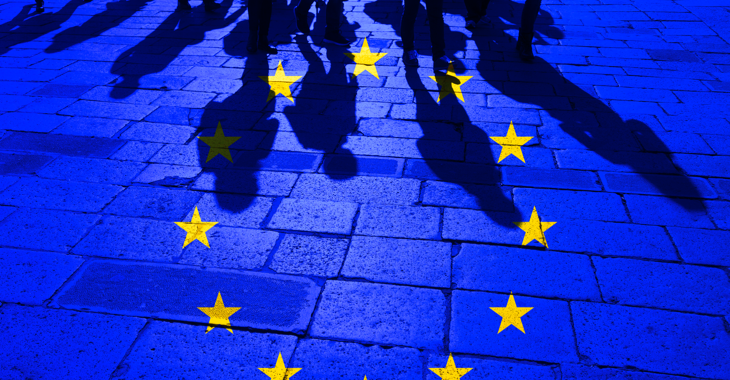 EU-Flagge über Menschenschatten Pflastersteinen © iStock/robertiez