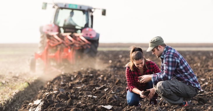 Eine Bäuerin und ein Bauer vor einem Traktor mit Pflug auf einem umgepflügten © FeldiStock/fotokostic