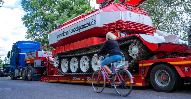 Waldbrand in Lübtheen in Mecklenburg-Vorpommern: Eine Frau fährt mit einem Fahrrad an einem Tieflader mit einem Feuerlöschpanzer vorbei © dpa/Jens Büttner