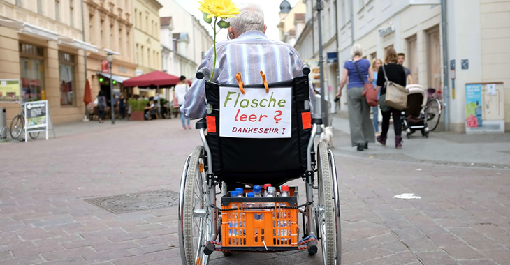 Ein älterer Mann in einer Fußgängerzone hat an seinem Rollstuhl einen Zettel befestigt mit der Aufschrift »Flasche leer? Danke sehr!« befestigt © dpa« Ein älterer Mann in einer Fußgängerzone hat an seinem Rollstuhl einen Zettel befestigt mit der Aufschrift »Flasche leer? Danke sehr!« befestigt © dpa