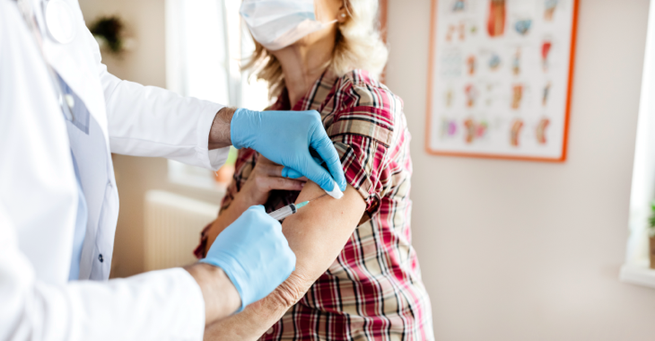 Eine Frau mit Mundschutz wird geimpft © iStock/PixelsEffect