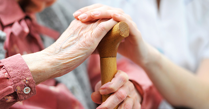 Hand einer Frau auf der Hand einer älteren Frau mit einem Gehstock