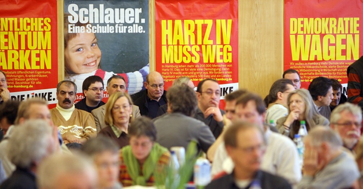 Ein Plakat mit der Aufschrift »Hartz IV muss weg« vor einer Menschengruppe © picture-alliance/dpa|Jens Ressing