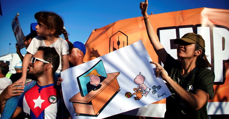 Bei der 1.Mai-Demo 2019 in Kubas Hauptstadt Havanna halten Teilnehmer eine Zeichnung, auf dem ein Kleinkind seinem Spielzeugbär die Augen zuhält, damit er Donald Trump nicht im Fernsehen sehen muss © REUTERS/Alexandre Meneghini