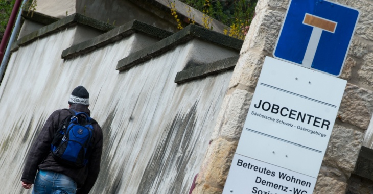 Ein Mann läuft an einem Sackgassen-Schild, das über einem Jobcenter-Schild angebracht ist, vorbei © Arno Burgi/dpa