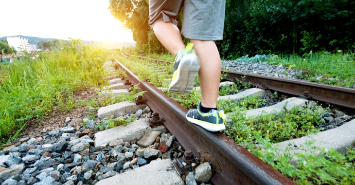 Ein Junge balanciert auf stillgelegten, mit Unkraut bewachsenen Bahngleisen © iStock/baona