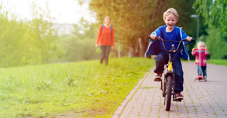 Eine Mutter mit ihrem Sohn auf einem Fahrrad und ihrer Tochter auf einem Tretroller © iStockphoto.com/Nadezhda1906