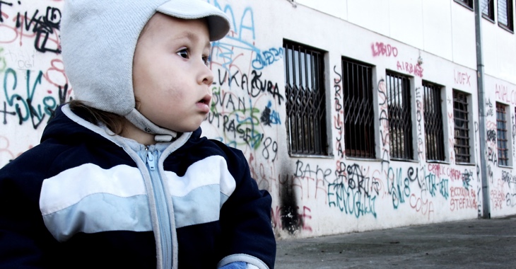 Ein Kind vor einem Haus mit Graffiti an der Wand und Gittern vor den Fenstern © iStock/brunette Ein Kind vor einem Haus mit Graffiti an der Wand und Gittern vor den Fenstern © iStock/brunette