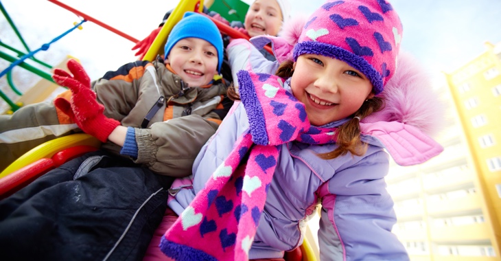 Drei Kinder im Winter auf einem Spielplatz © iStock/shironosov