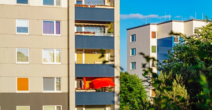 Mehrfamilienhäuser im Plattenbau-Stil mit einem roten Sonnenschirm auf einem Balkon © iStock/deepblue4you