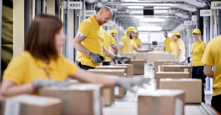 Arbeiter:innen in einem Logistikunternehmen verpacken an einem Fließband Pakete @ iStock/simonkr