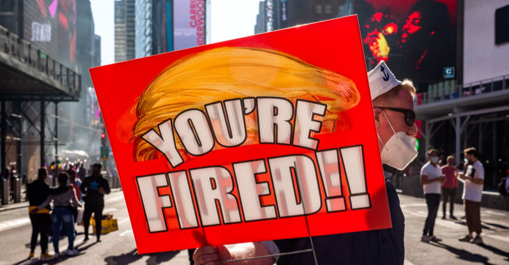 Ein Mann auf dem Times Square in New York hält ein Schild mit stilisierter oranger Trump-Frisur und der Aufschrift: You're fiert! © picture alliance/ZUMAPRESS.com/Milo Hess