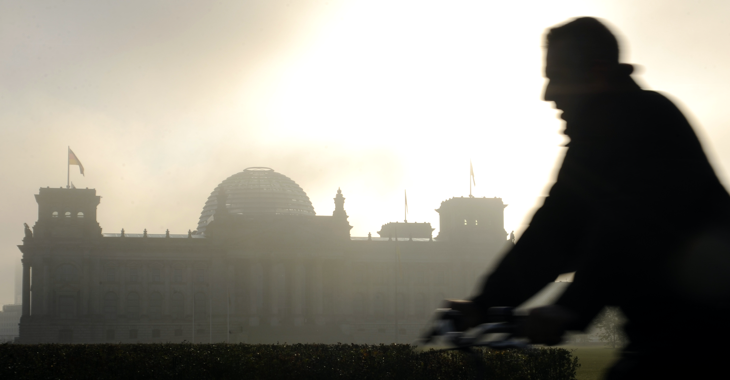 Silhouette eines Fahrradfahrers vor dem Reichstagsgebäude in Morgendunst mit dahinter aufgehender Sonne © picture-alliance/dpa/Rainer Jensen