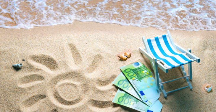 Strand mit Wasser, einer Sonne in den Sand gezeichnet und drei 100-Euro-Scheinen neben einem Liegestuhl © iStock/AlexRaths Strand mit Wasser, einer Sonne in den Sand gezeichnet und drei 100-Euro-Scheinen neben einem Liegestuhl © iStock/AlexRaths