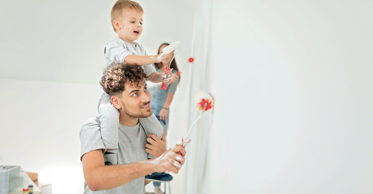 Eine Junge Familie beim Malern ihrer Wohnung, der Sohn mit Farbrolle auf den Schultern des Vaters © iStock/aywan88