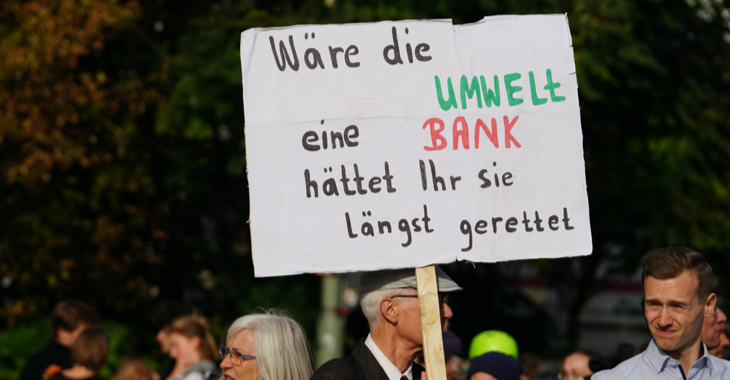 Ein Demonstrationsteilnehmer trägt ein Schild mit der Aufschrift: Wäre die Umwelt eine Bank, hättet ihr sie längst gerettet.