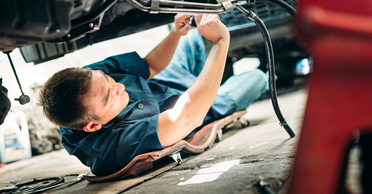 Mann liegt seitlich auf einem Rollbrett und arbeitet am Unterboden eines Autos © istockphoto.com/ferrantraite Mann liegt seitlich auf einem Rollbrett und arbeitet am Unterboden eines Autos