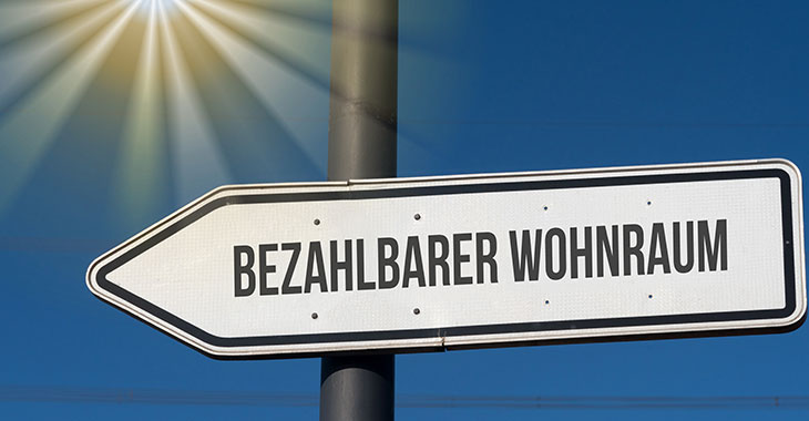 Schild mit der Aufschrift "Bezahlbarer Wohnraum" vor blauem Himmel