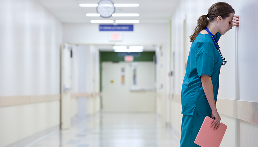 Eine erschöpfte Pflegekraft lehnt an der Wand eines Flurs im Krankenhaus. Foto: istock.com/FangXiaNuo Eine erschöpfte Pflegekraft lehnt an der Wand eines Flurs im Krankenhaus. Foto: istock.com/FangXiaNuo
