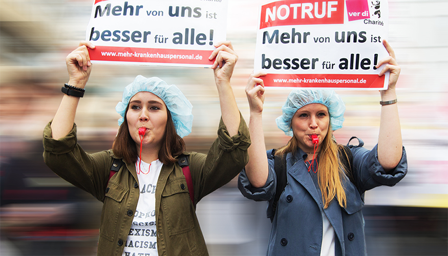 Berliner Pflegekräfte beim Pflegestreik der Charité halten Schilder hoch mit dem Slogan "Mehr von uns ist besser für alle!"