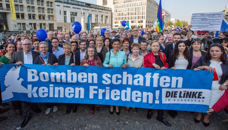 Bei der Friedenskundgebung am 18. APril 2018 am Brandenburger Tor in Berlin für Deeskalation in Syrien halten Mitglieder der Linksfraktion ein Transparent mit der Aufschrift: Bomben schaffen keinen Frieden!