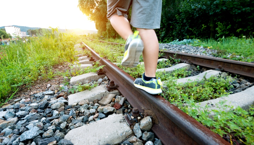 Ein Junge balanciert auf stillgelegten, mit Unkraut bewachsenen Bahngleisen © iStock/baona