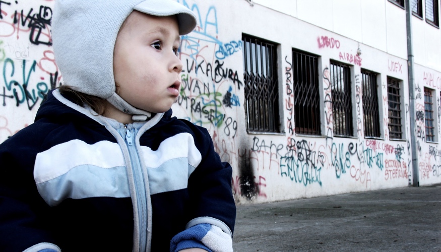 Ein Kind vor einem Haus mit Graffiti an der Wand und Gittern vor den Fenstern © iStock/brunette Ein Kind vor einem Haus mit Graffiti an der Wand und Gittern vor den Fenstern © iStock/brunette