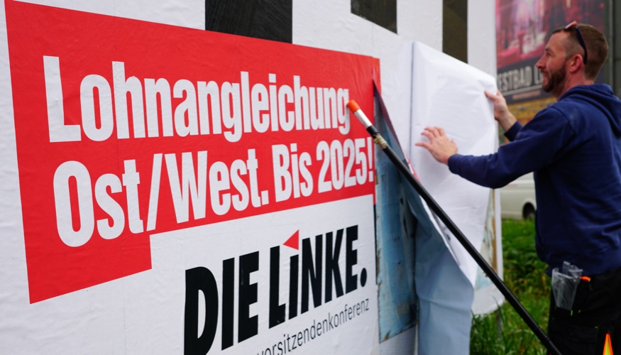 Ein Arbeiter bringt am 2. Mai 2019 in Leipzig eine Großfläche an mit der Aufschrift: »1:1 - Lohnangleichung Ost/West. Bis 2025!« © Olaf Krostiz